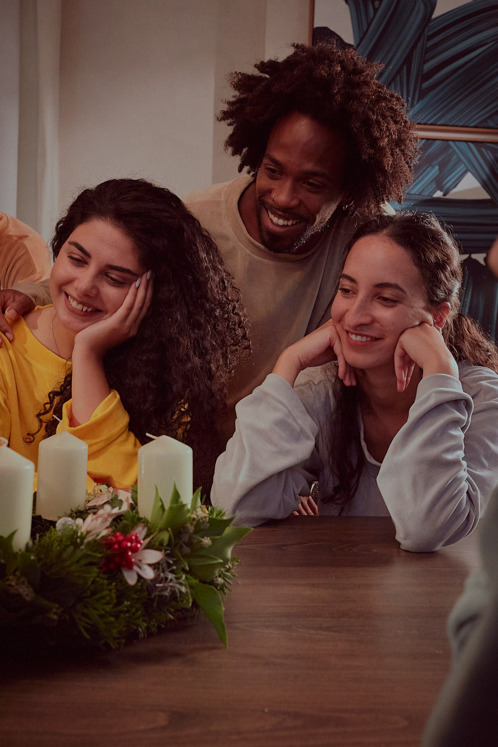 Drei Freundinnen und Freunde in Sonus Aeris Unisex Einteilern sitzen am Tisch mit Adventskranz cozy nachhaltige Loungewear fuer Feiertage und Zuhause