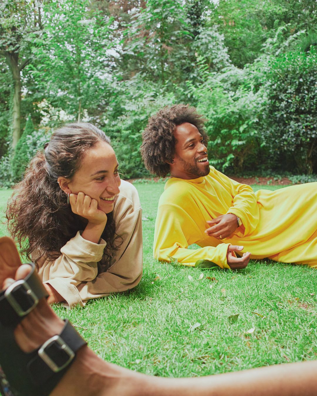 Couple wearing Sonus Aeris unisex one-pieces relaxing on green grass