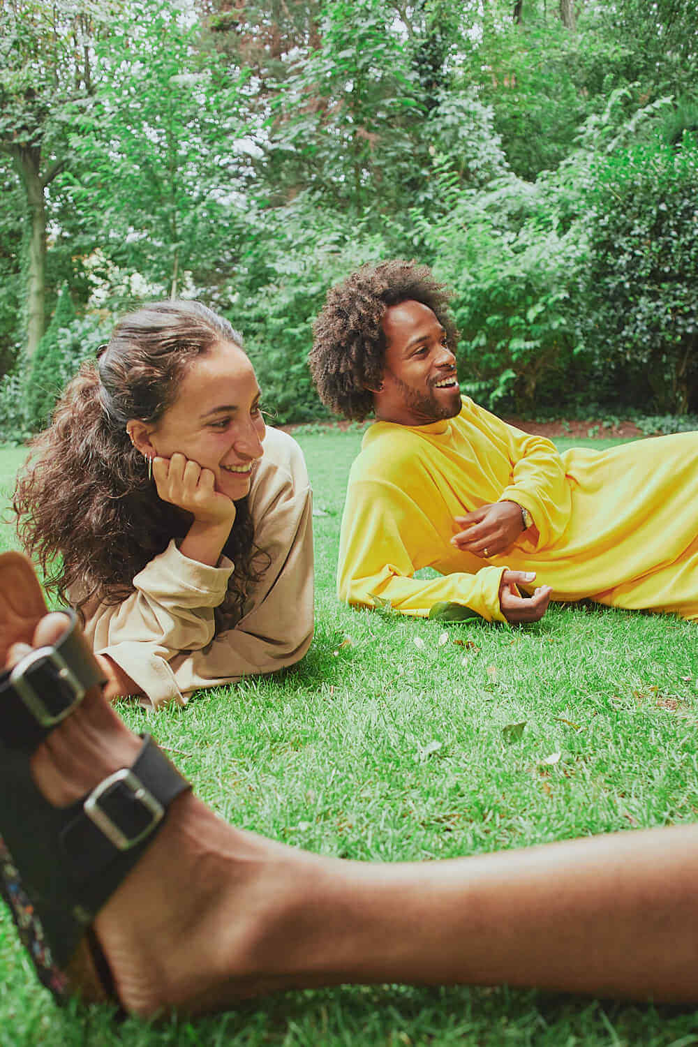 Couple wearing Sonus Aeris unisex one-pieces relaxing on green grass