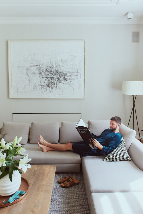 Man in deep petrol Sonus Aeris one-piece reading on the sofa