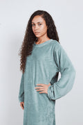 Woman in sage green Sonus Aeris one-piece against light background