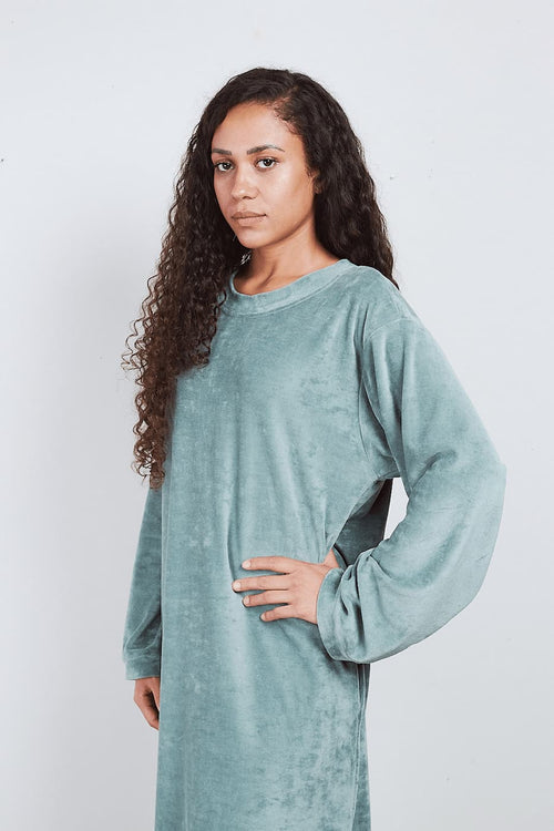 Woman in sage green Sonus Aeris one-piece against light background